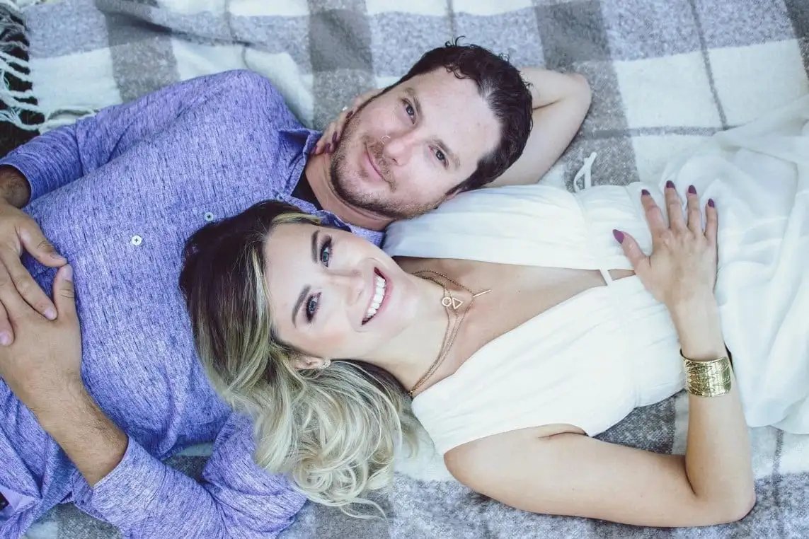 A couple lying on a plaid blanket, smiling up at the camera