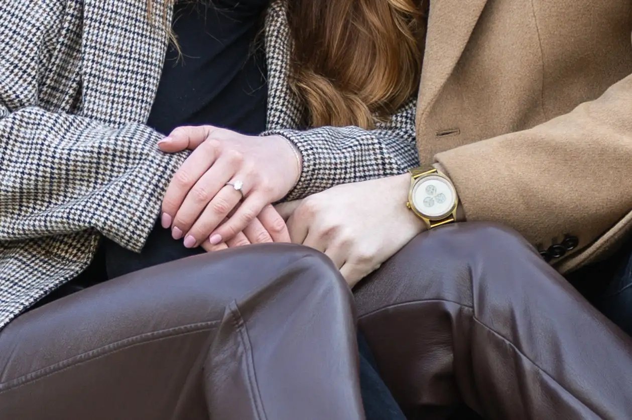 Close detail of a couple's clasped hands, engagement ring and watch catching the light