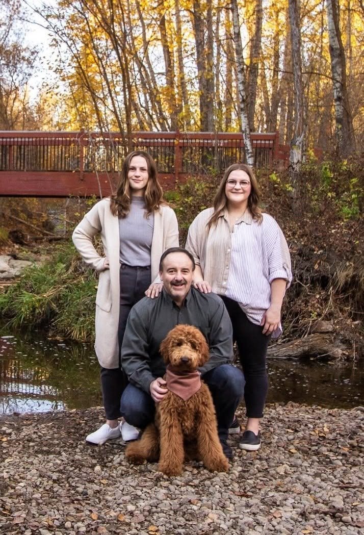 A family of four with their goldendoodle beside a red bridge in autumn